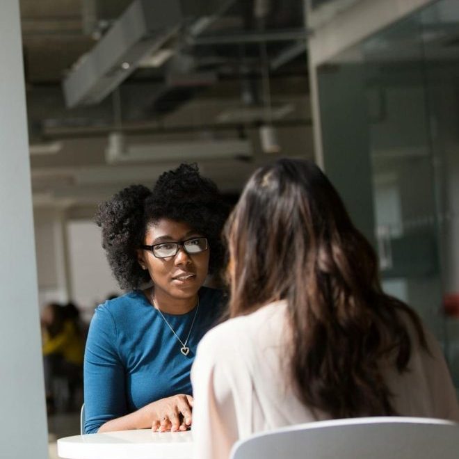 Two women engaged in a discussion in a modern office environment, highlighting communication and interaction.