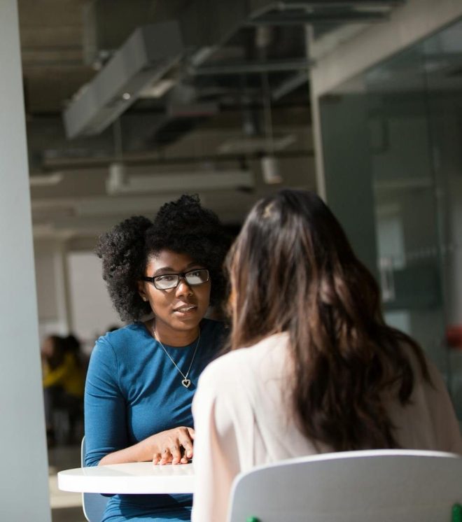 Two women engaged in a discussion in a modern office environment, highlighting communication and interaction.